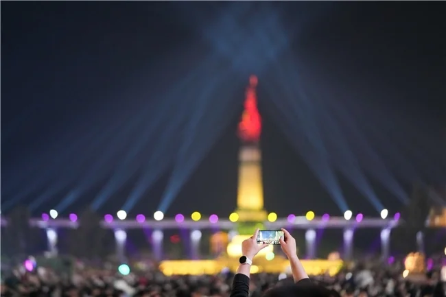 人们在哈尔滨人民防洪胜利纪念塔广场观赏、拍摄光影秀。（新华社图库/图）